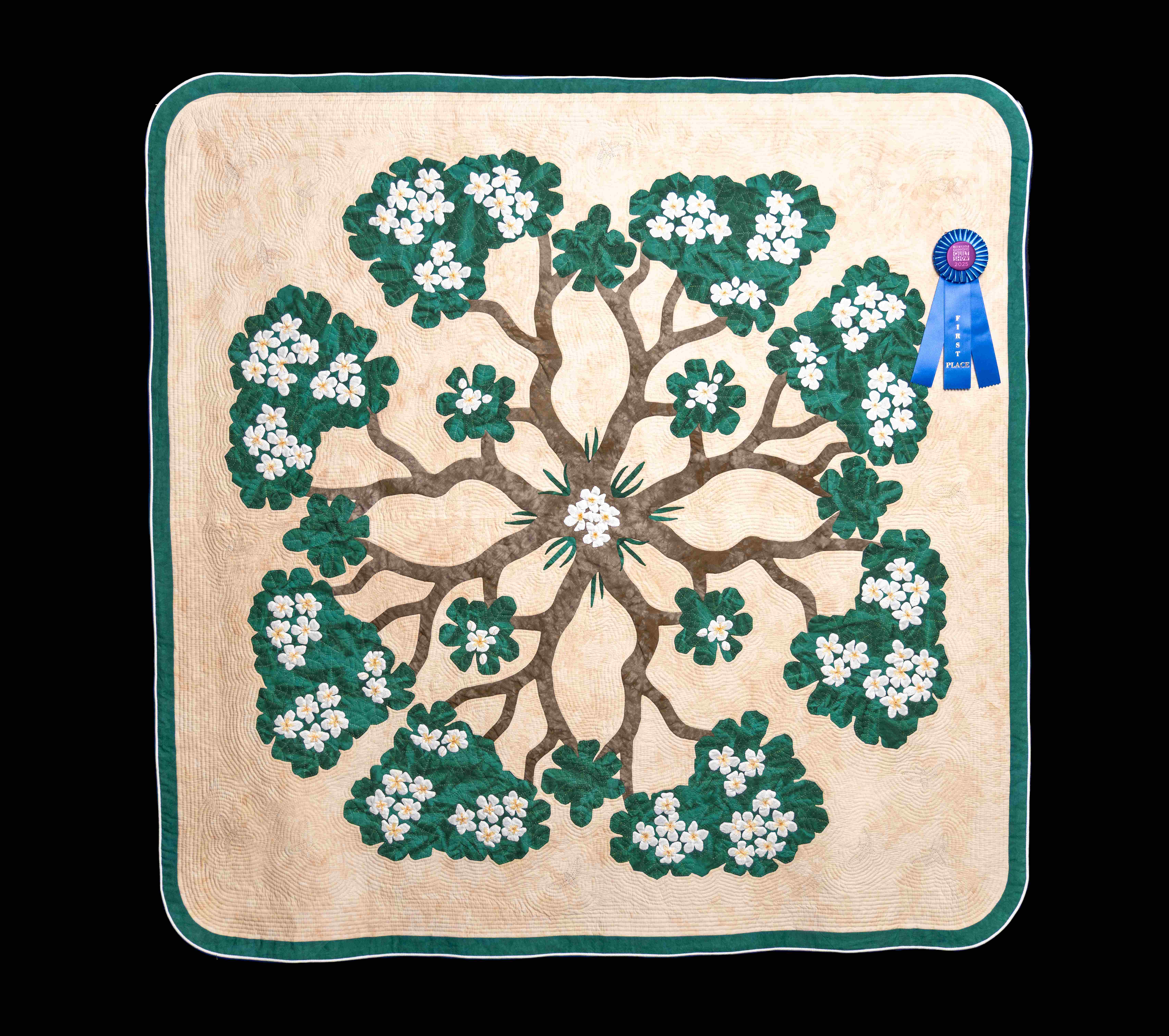 Award-winning quilt with radial tree branches, green foliage, and white flowers on beige—framed by green trim and centered with a circular floral design.