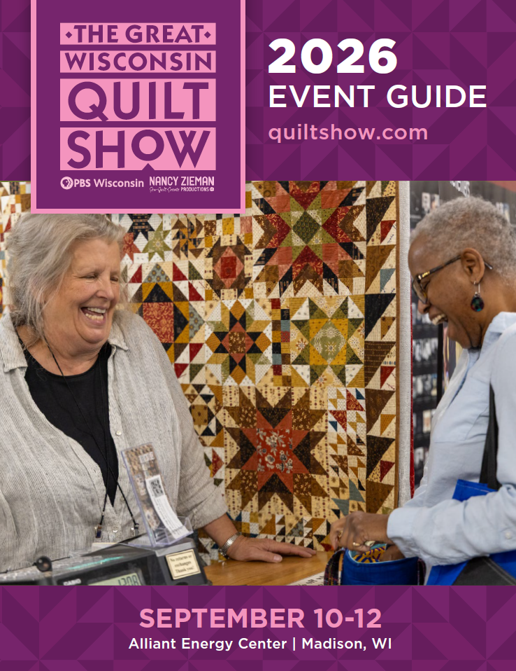 two women standing in front of quilts